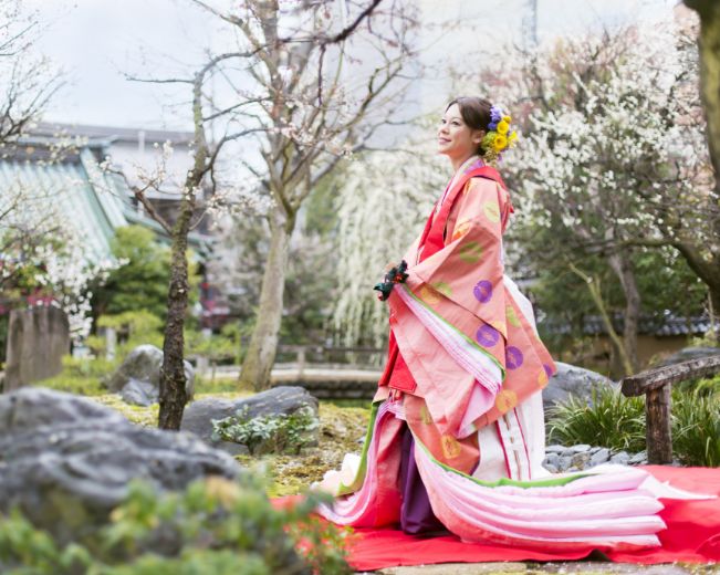 桜の咲く庭園で空を見上げる十二単を着た女性